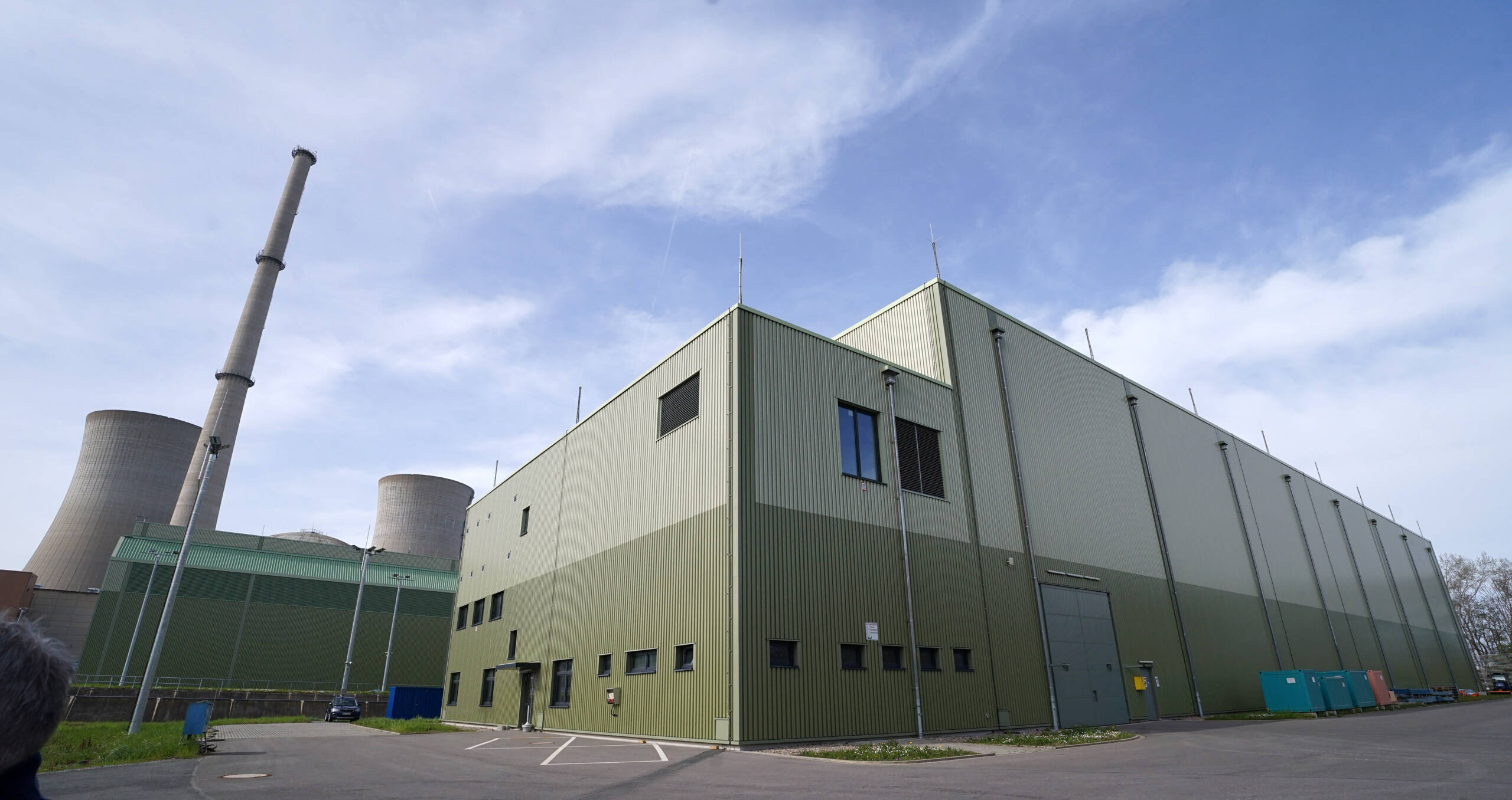 In dem Zwischenlager für hochradioaktive Abfälle (im Vordergrund) lagern die ehemaligen Brennelemente des Atomkraftwerks Grafenrheinfeld in blauen "Castoren", den Zwischenbehältern. Im Hintergrund links die beiden Kühltürme, die im Rahmen des Rückbaus am 16. August 2024, 18:30 Uhr gesprengt werden sollen. Foto: Heinz Wraneschitz