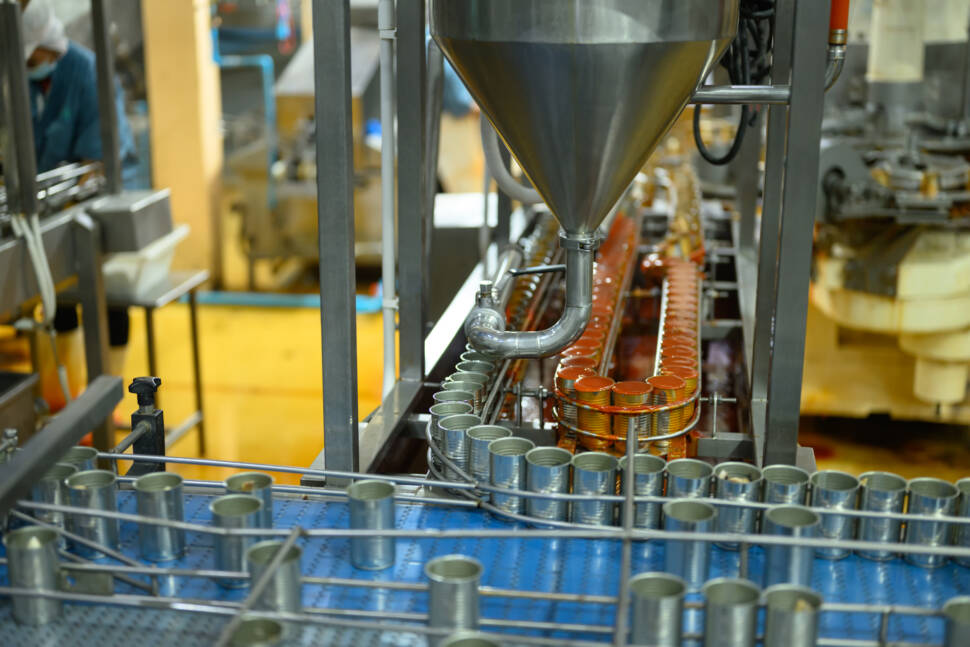 Automated factory line filling metal cans with food product in an industrial processing plant