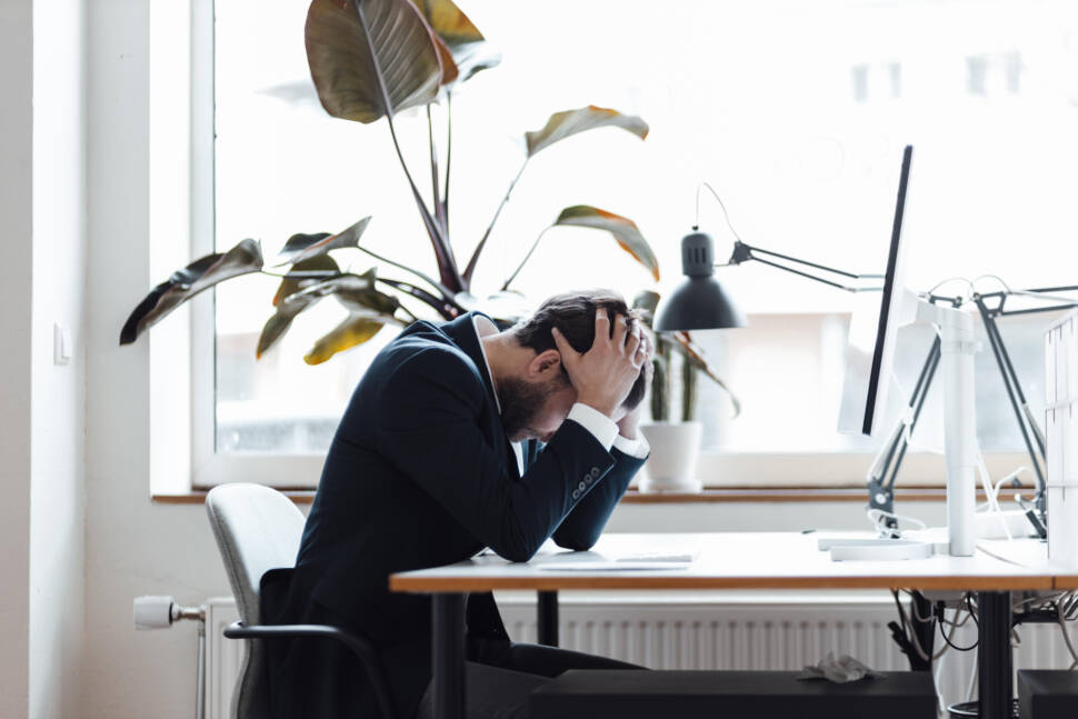 Male entrepreneur with head in hands sitting by desk at office
