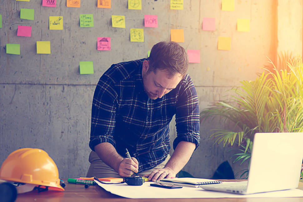 Young architecture or engineer working in office with laptop, lifestyle concept. Sticky notes on cement wall background.