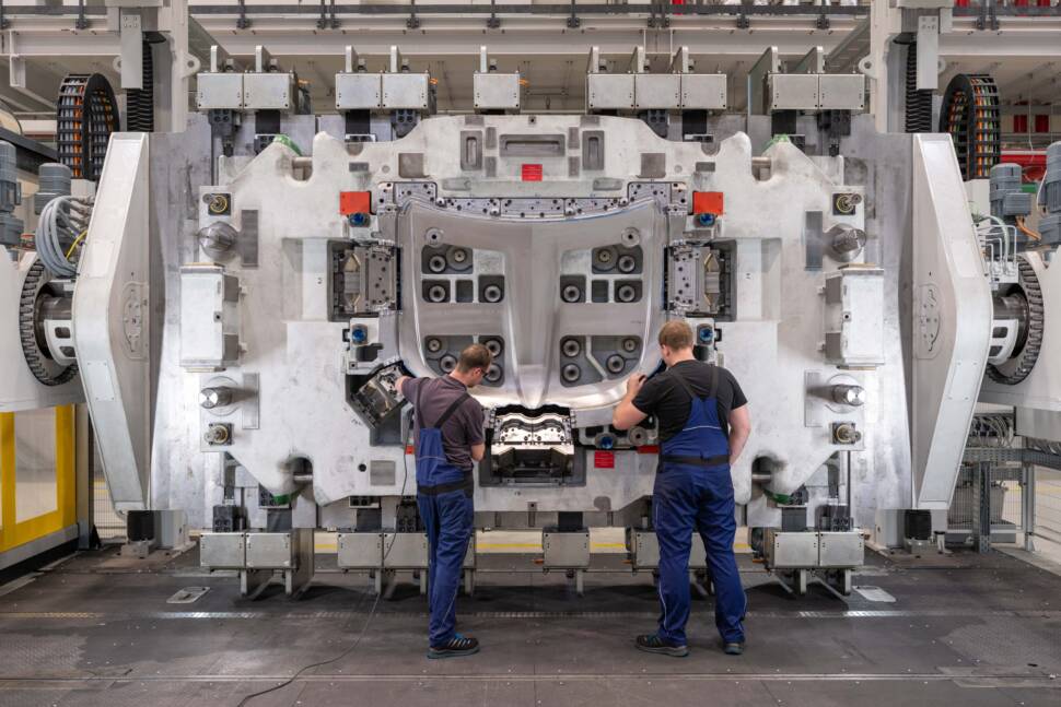 Zwei Mitarbeitende bei BMW stehen vor einem großen Umformwerkzeug.