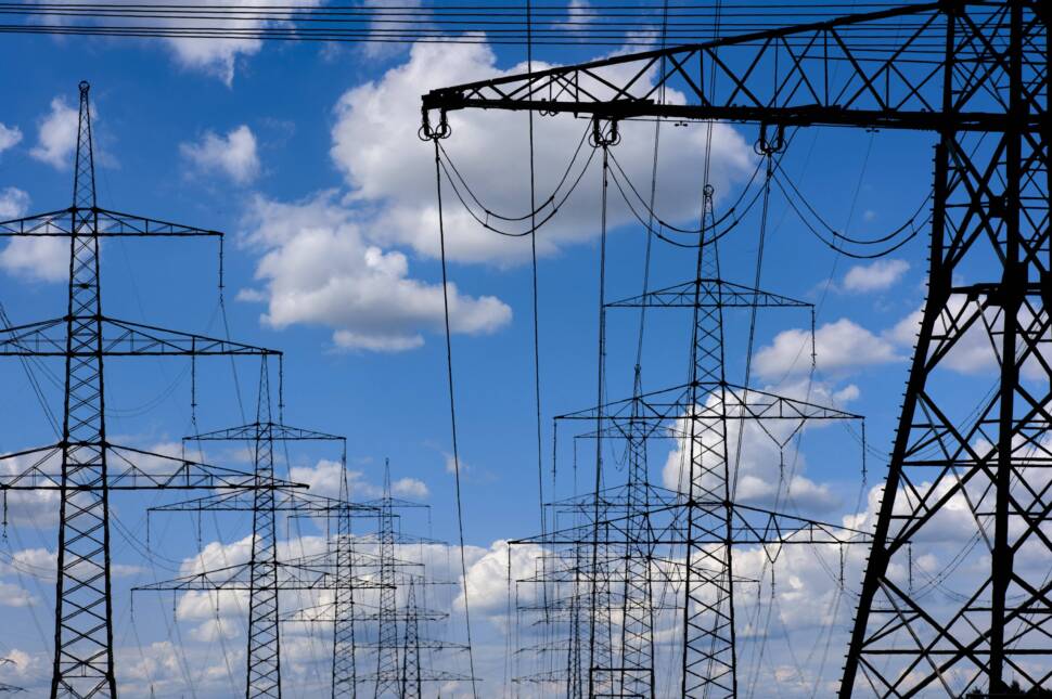 Hochspannungsmasten stehen vor einem Himmel mit dramatischen Wolken als Symbolbild für die Infrastruktur der Energieversorgung durch Elektrizität.