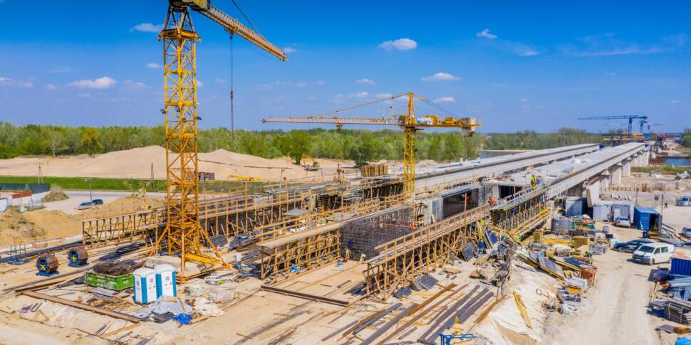 Luftaufnahme einer Baustelle einer neuen Brücke mit großem gelbem Kran im Vordergrund