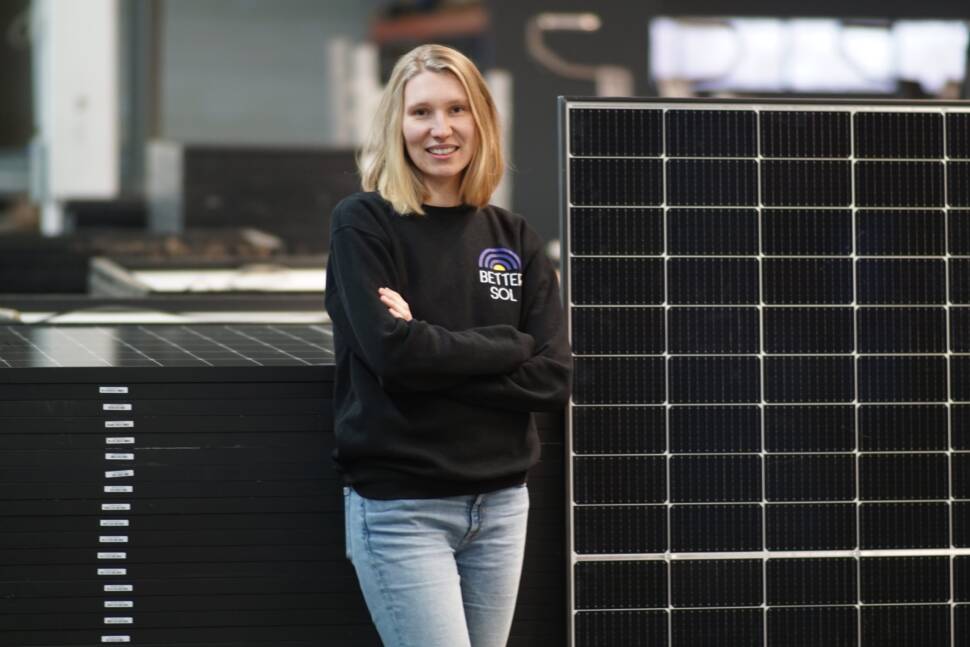 Luisa Schulze, Gründerin von Better Sol, neben einem stehenden Solarmodul, vor einem Stapel liegender Module