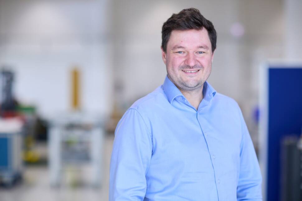 Uwe Bau, neuer CEO Gauss Fusion, im blauen Hemd vor Laborhintergrund.
