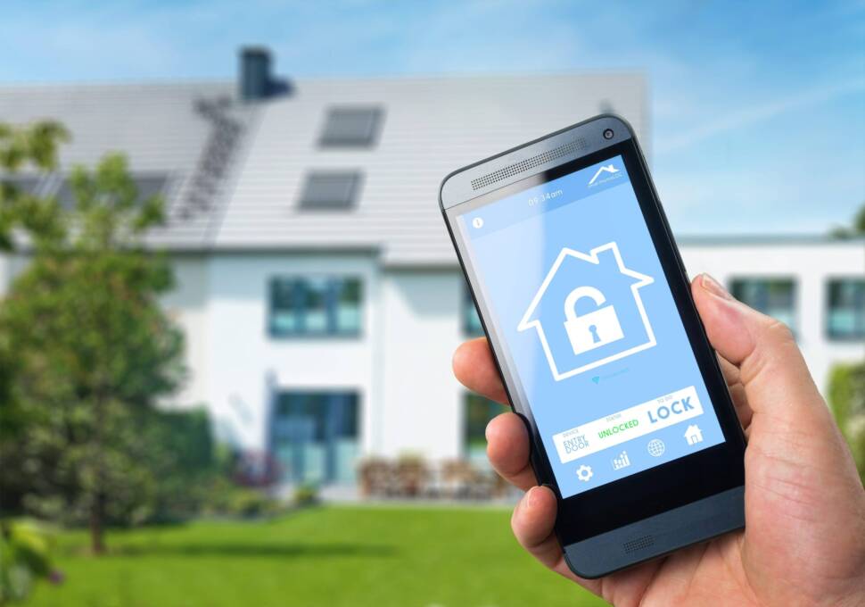 Hand mit Smartphone vor Haus, Symbolbild für Smart Home