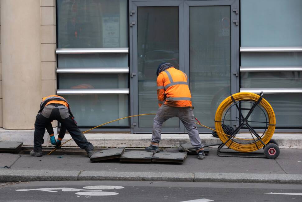 Arbeiter ziehen Schutzrohre für Glasfaserkabel in den Boden.